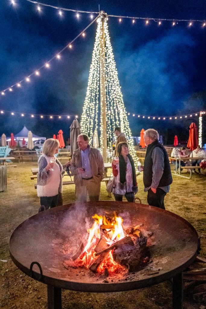 Families gathered around a crackling fire pit under a lit Christmas tree at Splashway Campground